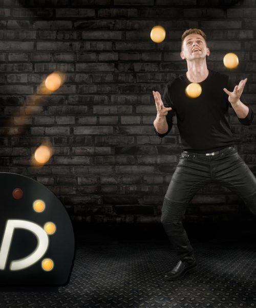 Niels juggling yellow balls in front of a brick wall